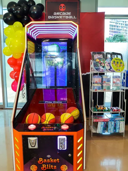 An arcade basketball machine set up for a Deadpool-themed party, complete with themed branding and prizes nearby.
