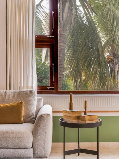 In this living room, the goal was openness. The large window brings the lush outdoors in, and the color palette of light wood and soft greens creates a serene atmosphere. A simple side table with books and decor adds a personal touch.