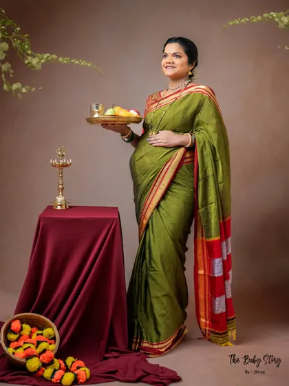 In this shot, the mother-to-be holds a thali of offerings, a beautiful custom in Indian culture. The composition, with marigold flowers at her feet, adds to the festive and sacred feel of the maternity portrait.