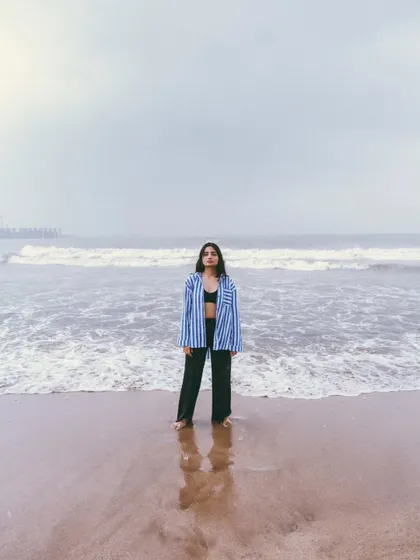 A wide shot emphasizing the solitude of the model against the vastness of the ocean. The reflection on the sand adds a beautiful symmetry.