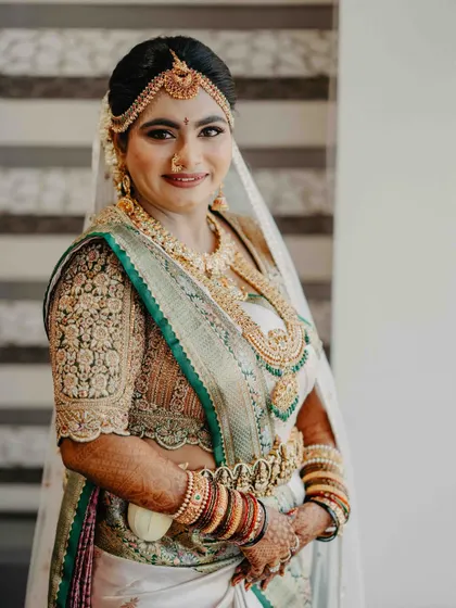A portrait of our stunning bride wearing a custom-designed blouse with her white and green silk saree. The intricate floral embroidery on the blouse sleeves is a work of art, perfectly complementing her traditional gold jewelry.
