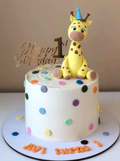 A simple and sweet first birthday cake with a cute giraffe topper and colorful polka dots.