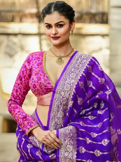 A vibrant pink brocade blouse with a deep V-neck and full sleeves. This is a statement piece that pairs beautifully with rich silk sarees like this purple Banarasi.