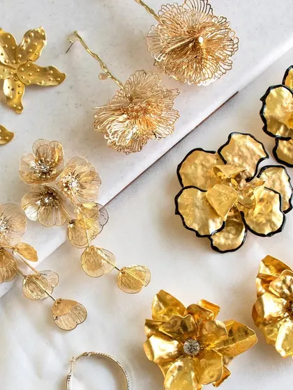 A closer crop of the statement earring flat lay, focusing on the intricate details of the textured flower drop and chunky metallic flower earrings.