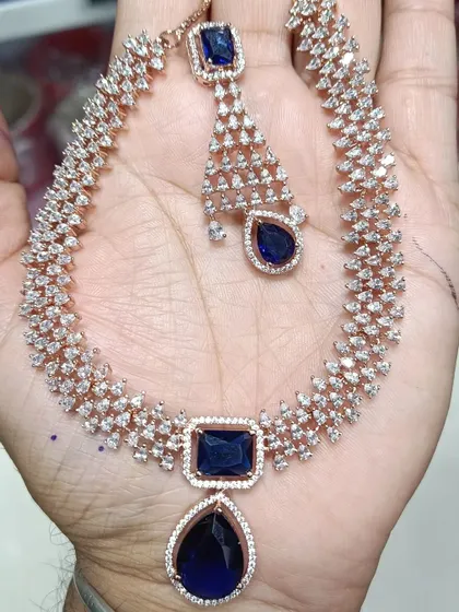A beautiful American Diamond necklace set with a large sapphire-blue stone. This set comes with matching earrings and a maang tikka, offering a complete, modern look for any party.