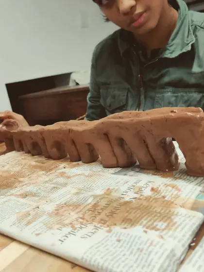 A student carefully constructs a long, arched structure during a kids pottery workshop. This kind of project helps develop fine motor skills and patience, all while having fun with a natural material.