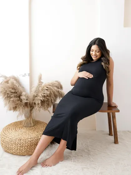 A relaxed and happy portrait in a simple black dress. The mom-to-be is seated in a modern boho setting, her smile radiating pure joy.