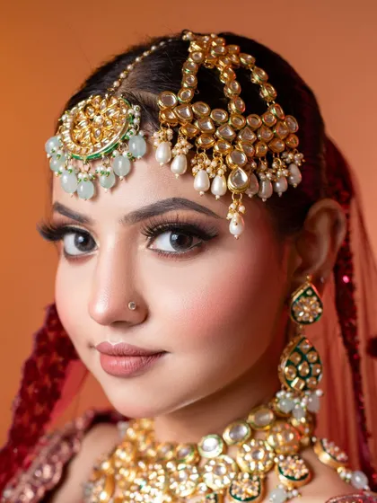 A detailed view of a bridal makeup look, showcasing precision in the eye makeup and the intricate design of the jewellery. The combination of a double maang tikka with pearl and mint green beadwork demonstrates our extensive and high-quality accessory collection.