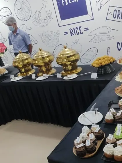 A wide view of our dessert and snack counter at a corporate party. The spread includes a variety of cupcakes, Indian sweets like ladoo, and other baked goods.