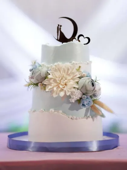 This two-tier engagement cake was crafted to perfectly match the couple's outfits and the event's decor. The soft blue and white tones, combined with a large dahlia and a moon topper, create a dreamy, celestial vibe.