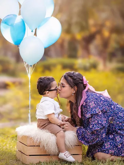 A mother's kiss for her little boy during an outdoor session. The natural light and green background create a fresh and vibrant family photo.
