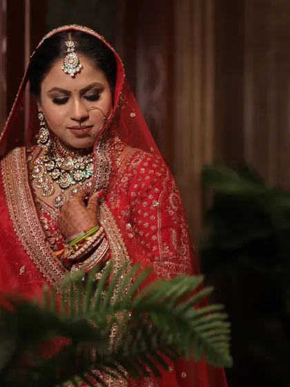 A beautiful color portrait of the bride, her red lehenga standing out against the lush green plants, capturing her serene beauty.