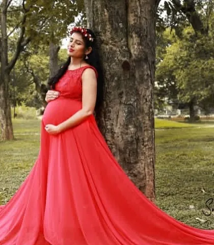 This simple yet elegant red maternity gown with a long trail is perfect for outdoor photoshoots in a natural park setting.