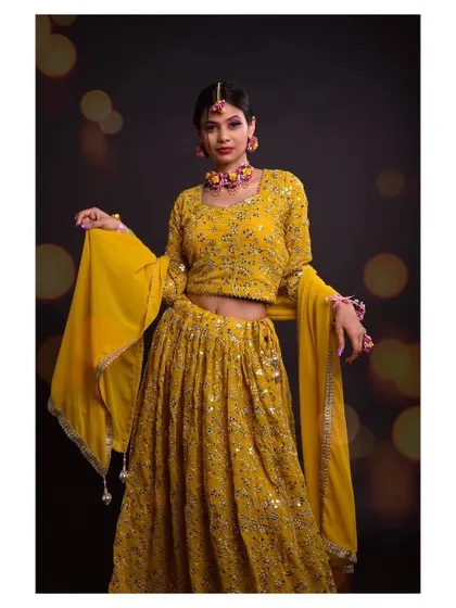 A full-length shot of a model in a beautiful yellow lehenga. The bokeh background adds a festive and magical touch.