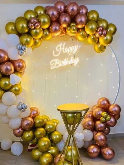 A sophisticated birthday balloon ring in metallic gold, rose gold, and white, with a neon sign and a cake pedestal.