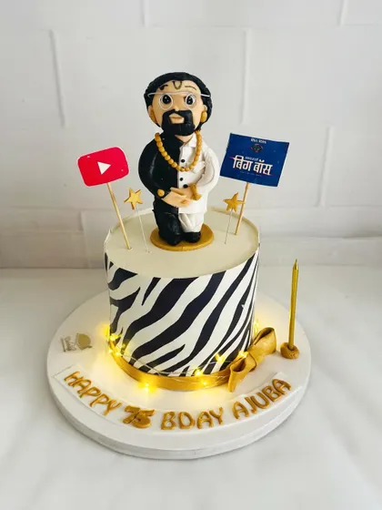 A fun and trendy cake for "Ajuba" (grandfather), with a zebra print tier and toppers representing his interests like YouTube and Bigg Boss.