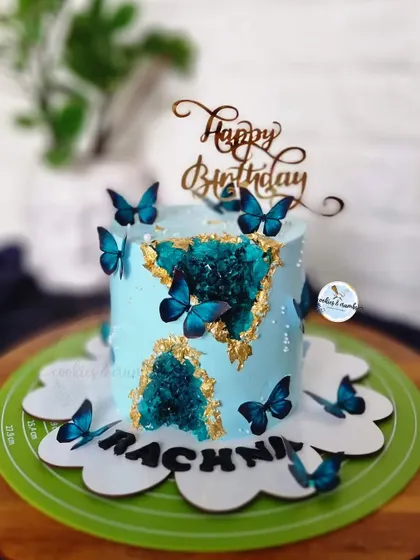 A geode cake with a twist. The deep teal crystals and royal blue butterflies create a stunning contrast against the light blue buttercream, making it a true work of art.