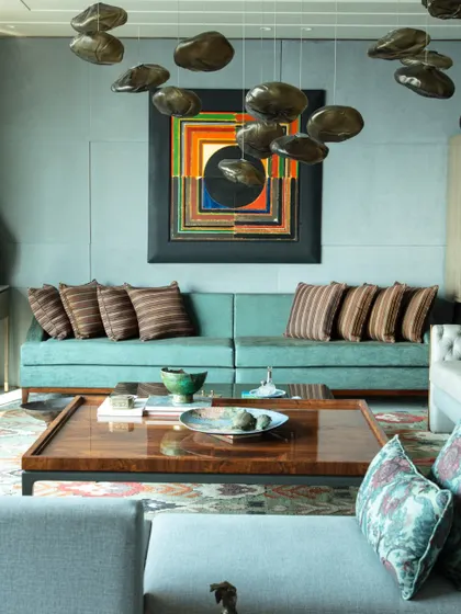 A wide shot of the living room, highlighting the large S.H. Raza painting and the 'Bocci clouds' light installation. The room is a perfect example of maximalist design, executed with elegance and artistic flair.