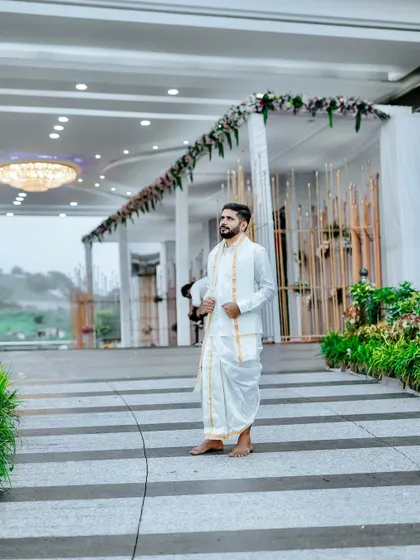 The groom looking sharp at his wedding muhurtham. The decor in the background features a clean, elegant floral arch over the entrance to the main hall.