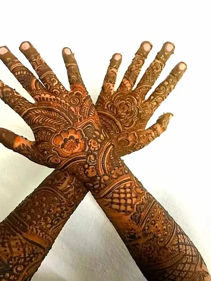 A beautiful pose showcasing a full bridal henna design. The crossed hands highlight the intricate patterns on the arms and the detailed work on the fingers.