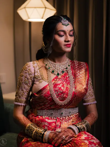 A serene portrait of a bride in her magnificent red and gold wedding saree. The focus is on her peaceful expression and the incredible detail of her diamond jewelry.