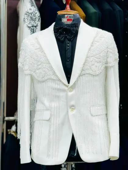 A full view of the white tuxedo with fringe detailing. The dramatic sleeves and unique silhouette make this a one-of-a-kind couture piece.