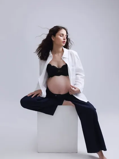 A confident and stylish pose. Seated on a simple white block, the mom-to-be's modern outfit and strong posture create a striking and fashionable maternity portrait.