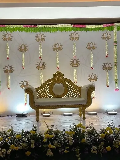 An elegant and simple stage with a lotus theme. The hanging lotus cutouts and a classic golden sofa create a serene and traditional look, perfect for an engagement.
