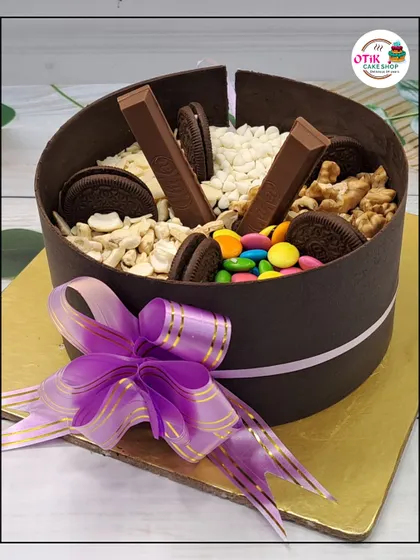 This unique "smash" cake is a chocolate shell filled with more treats inside. It's decorated with KitKats, Oreos, gems, and nuts, making it a fun and interactive dessert.