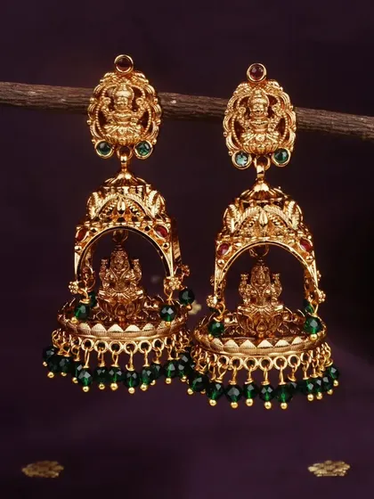 This pair of traditional jhumkis is finished with deep green beads, offering a beautiful contrast against the matte gold. The Lakshmi motif adds a divine touch.