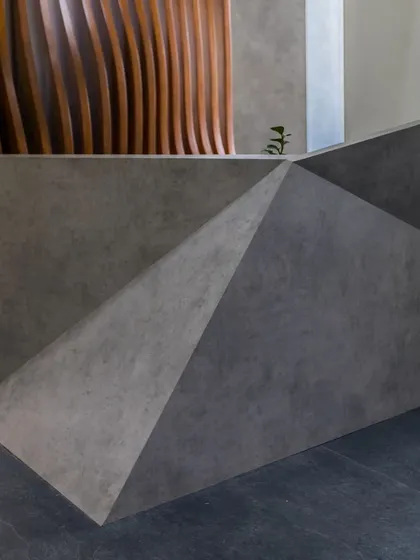 A detail from the 'Acutely Bare' office space, showing a faceted, concrete-finish reception desk against a fluted wooden wall. This image highlights our focus on material junctions and custom-designed furniture as part of our interior architecture services.
