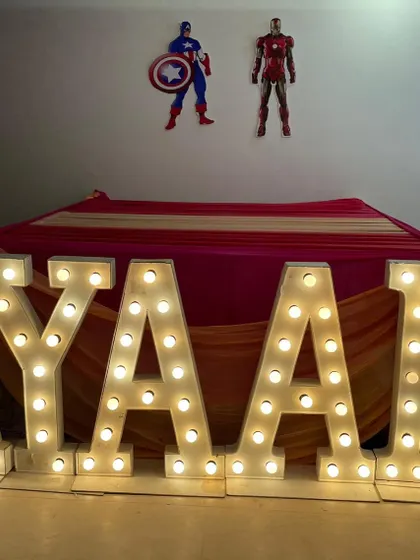 Large marquee letters for "AYAAN" with Avengers characters on the wall above, part of a superhero-themed party.