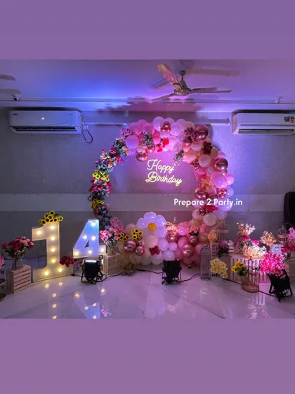 A vibrant and floral 14th birthday party. This setup features a full circular balloon arch decorated with colorful artificial flowers, a central neon sign, and large light-up marquee numbers.