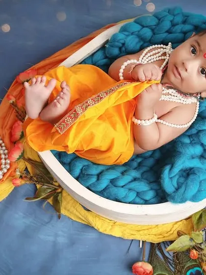 A full-length view of our little Krishna, showing his tiny feet. This pose, set against a celestial blue background, captures both divinity and innocence.