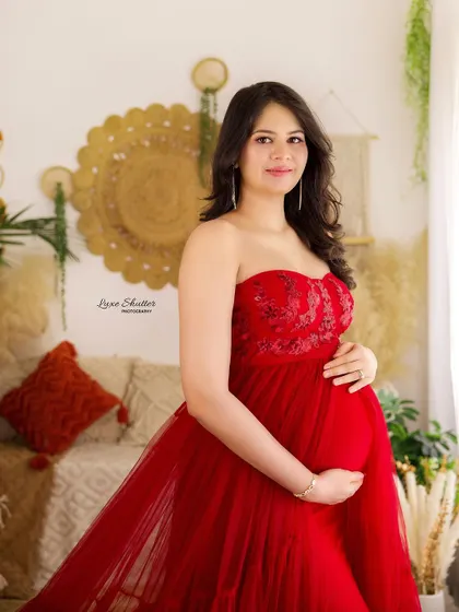 A close-up shot showcasing the beautiful details of the embroidered bodice on this red tulle gown. The soft, natural light highlights the mother's radiant glow.