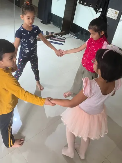 Four young students hold hands in a circle, getting ready for a group dance activity.