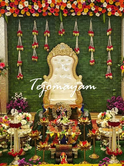 A baby shower setup with a backdrop of woven banana leaves and hanging flower garlands, creating a very traditional and natural look.