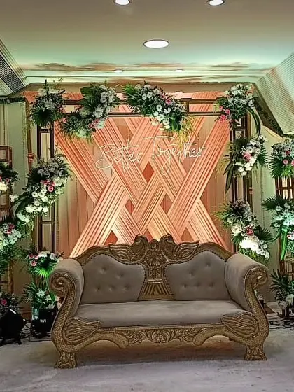 An elegant stage for an engagement or Roka ceremony. The backdrop features a creative weave of peach-colored drapes, floral arrangements, and a "Better Together" neon sign.