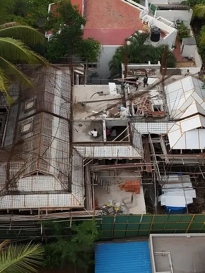A top-down drone view of a residential site, showing the complexity of the roof structure and the building's footprint amidst the trees.