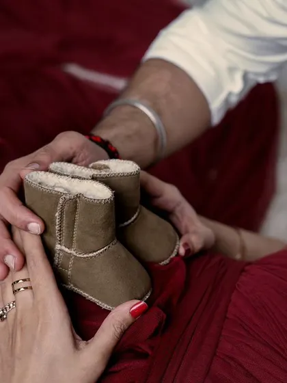 A close-up detail of an expecting couple holding a pair of tiny boots over the baby bump. These prop shots add a sweet and symbolic touch to your maternity photoshoot.