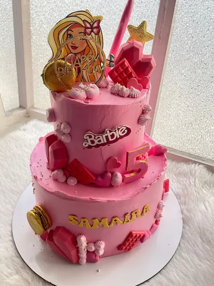 Come on Barbie, let's go party! A two-tier, all-pink Barbie cake for a 5th birthday, decorated with macarons, chocolate bars, and the iconic Barbie logo.