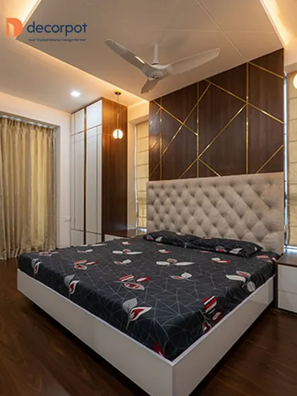 A luxurious bedroom design featuring a tufted beige headboard against a dark wood paneled wall with brass inlays. The combination of textures and materials creates a sophisticated and inviting atmosphere.