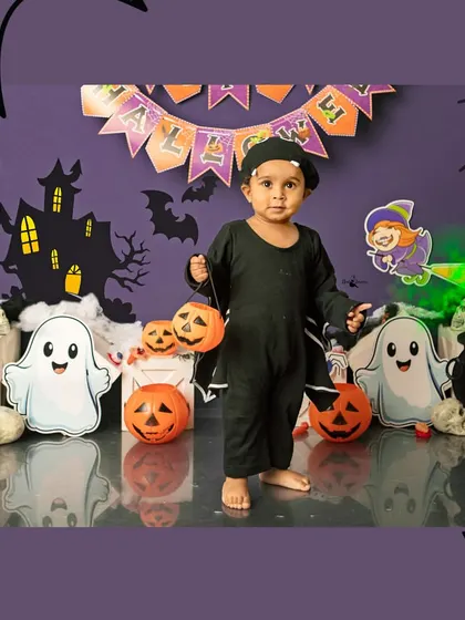 Trick or treat. A little one dressed as a bat holds pumpkin baskets in our Halloween setup, complete with ghosts and a haunted house.