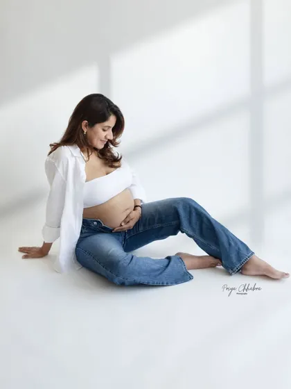 A quiet moment of reflection. This minimalist studio shot, with its clean background and casual styling, puts all the focus on the mother's peaceful connection with her baby bump.