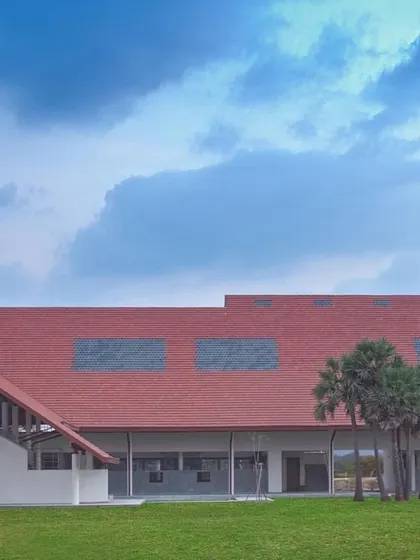 The long, sloping roof of an academic building at Vellore International School, set against a backdrop of palm trees and a bright blue sky.