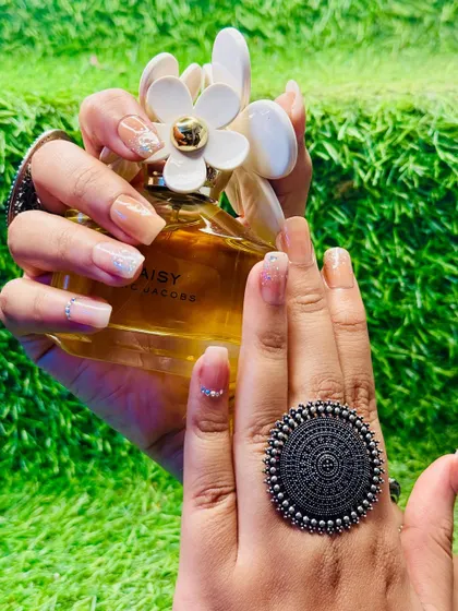 Here, the nude and glitter nail art is paired with a different accessory, showing its versatility. A delicate white floral design is added to one nail for a custom touch.