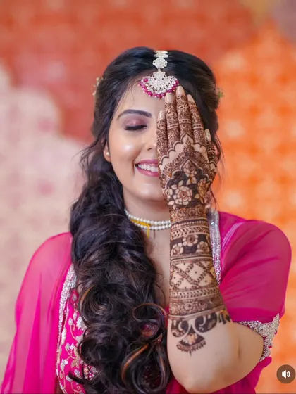 A joyful bride poses with her mehndi, her smile as bright as her henna. This is a classic pose that beautifully showcases the design on one arm.