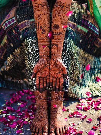 A classic bridal shot, with the bride's hands and feet adorned with intricate henna and surrounded by flower petals.