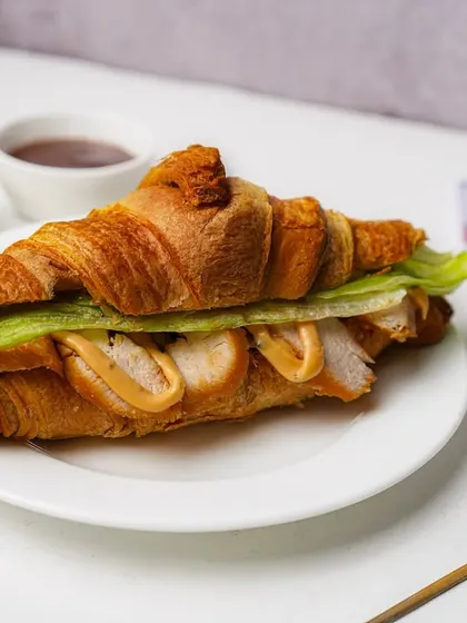 A flaky croissant sandwich filled with chicken and lettuce, showcasing a savory bakery item.