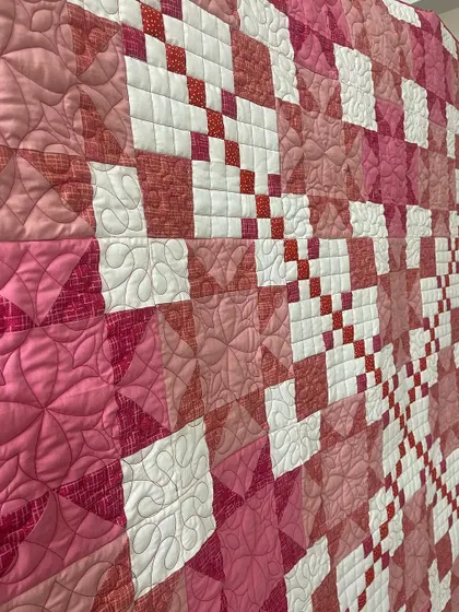 A detail shot of a pink Irish Chain quilt, showing the variety of quilting patterns used.